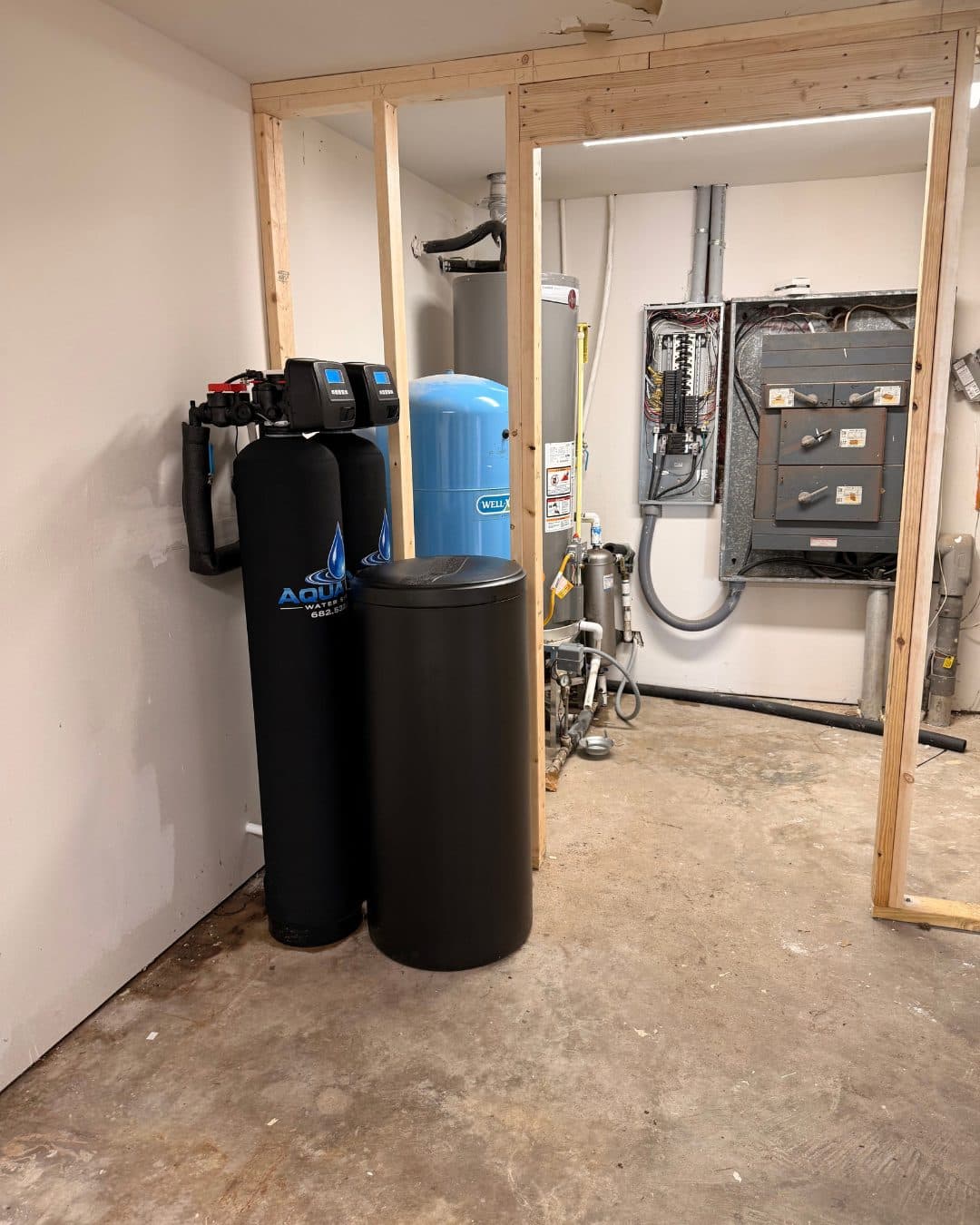 An Aqua One well water system installed beside a pressure tank and well pump in a utility room